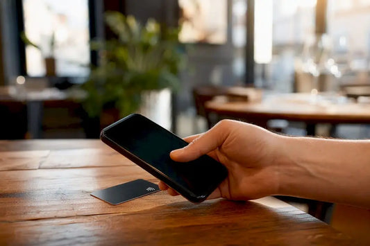 Eine Hand hält ein Smartphone an eine NFC-Karte am Kassentresen, um kontaktlos zu bezahlen.