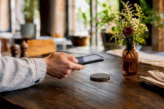 Hand tippt Smartphone mit NFC-Karte auf den Tresen