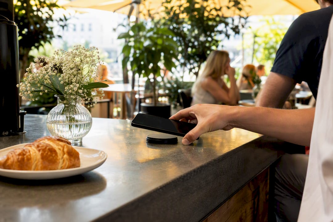 Hand tippt mit dem Smartphone auf den NFC-Tag an der Café-Theke